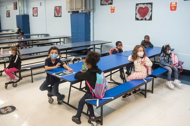 Several young students sit at a lunch table wearing masks at P.S. 188 The Island School.